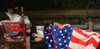 Imigrante dormindo na rua e usando bandeira americana como cobertor